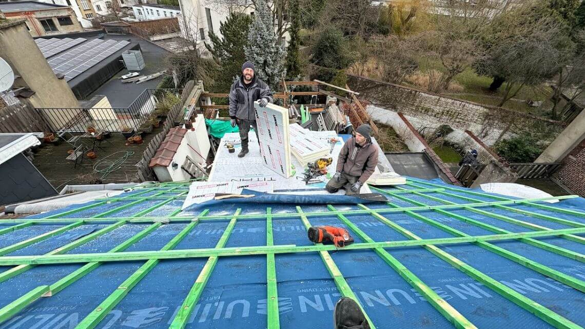 Couvreurs installant l’isolation d’une toiture inclinée, avec panneaux isolants et lattage vert visibles.